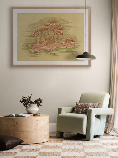 A cozy living room corner features a light green armchair, checkered rug, and Urban Road's "Gathering at Wattle Hollow" Light Green Framed Art Print depicting bushland trees on a pale wall. A round marble table with a vase and book sits beneath a black pendant light.
