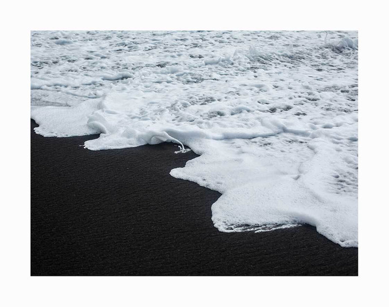 The Vik Unframed Art Print by Urban Road captures white sea foam gently washing onto the black sand of Vik’s beach, highlighting the dramatic contrast between frothy waves and smooth, dark shore.