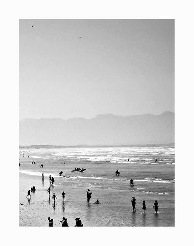 People enjoy the shoreline in this striking black and white scene titled "Summer Wave II Unframed Art Print" by Urban Road, featuring beachgoers, gentle ocean waves, a hazy sky, and distant mountains.