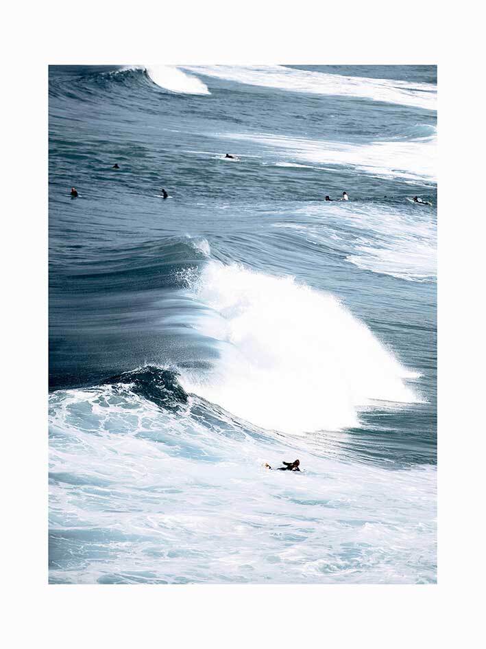 A group of surfers waits as one rides a powerful wave in this energetic ocean scene, depicted in the "Wipeout Unframed Art Print" by Urban Road.