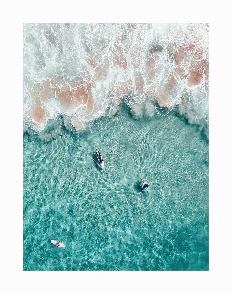 The Hang Ten Unframed Art Print by Urban Road captures an aerial view of three surfers in clear waters, waiting on their boards as white waves roll in—perfect for surf photography lovers.