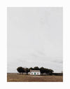 The Little Cottage Unframed Art Print by Urban Road features a small white cottage with a green door and tiled roof, set on a brown field before trees and a cloudy sky.