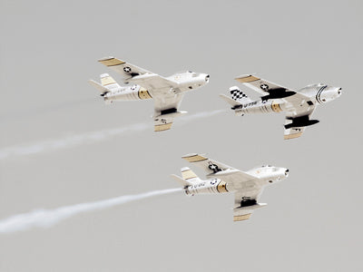 Three vintage military fighter jets soar in formation through a cloudy sky, leaving white trails. The Maverick Unframed Art Print by Urban Road is striking aviation décor—perfect wall art for enthusiasts and collectors alike.