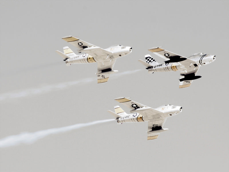 Three vintage military fighter jets soar in formation through a cloudy sky, leaving white trails. The Maverick Unframed Art Print by Urban Road is striking aviation décor—perfect wall art for enthusiasts and collectors alike.