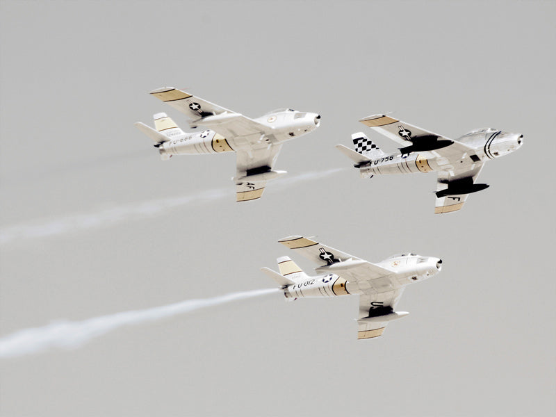 The Urban Road Maverick Unframed Art Print features three vintage military planes with white and beige markings flying in formation through a cloudy sky, leaving white smoke trails behind them.