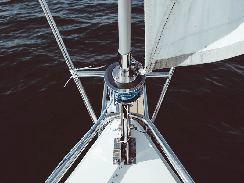 Experience the striking photographic image "Half Mast Unframed Art Print" by Urban Road, showcasing shiny metal railings, a furled headsail, and calm dark blue waters viewed from a boat’s bow.