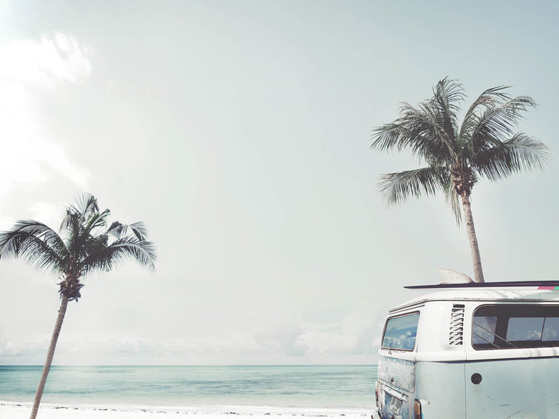 Good Vibrations Unframed Art Print by Urban Road features a vintage blue kombi van on a sandy beach near palm trees, with turquoise ocean and a pale, cloudy sky—the perfect beach wall art.