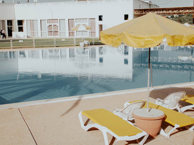 Summertime Sadness Unframed Art Print by Urban Road features a golden poolside with yellow lounge chairs and an umbrella, capturing serene relaxation as styled by Rachel Lynette French.