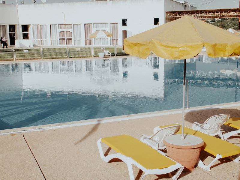 Summertime Sadness Unframed Art Print by Urban Road features a golden poolside with yellow lounge chairs and an umbrella, capturing serene relaxation as styled by Rachel Lynette French.