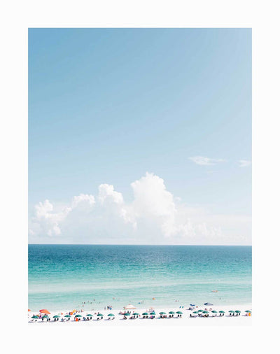 Vitamin Sea Unframed Art Print by Urban Road features a bright beach scene with colorful umbrellas, people relaxing on the sand, and swimmers in a turquoise ocean beneath white clouds and a clear blue sky.