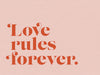 The Urban Road Love Rules Unframed Art Print features the phrase "Love rules forever" in red serif font on a light pink background, making a bold and stylish typographic statement for your space.