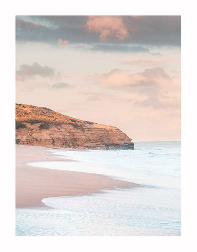 The Urban Road Sunset Beach Unframed Art Print captures gentle waves on sandy shores, a rocky cliff, and pastel clouds at sunset—an elegant photographic art piece that evokes calm and peace.