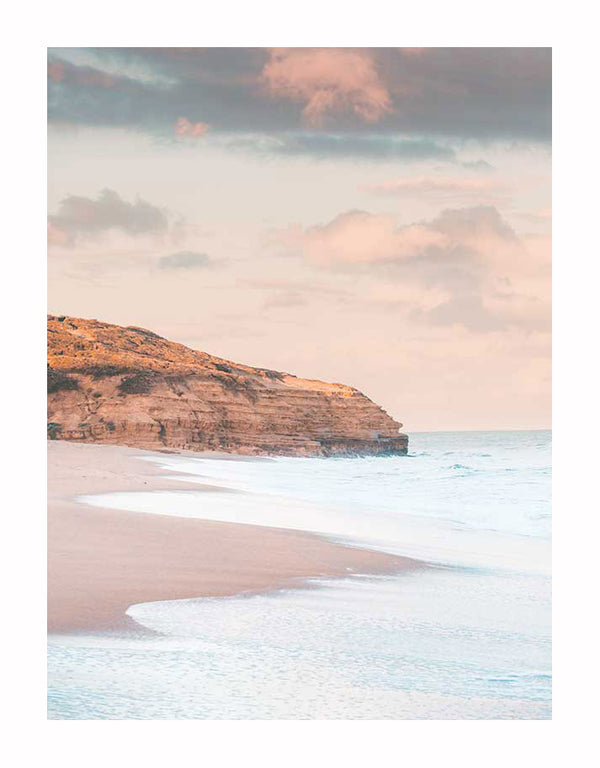 The Urban Road Sunset Beach Unframed Art Print captures gentle waves on sandy shores, a rocky cliff, and pastel clouds at sunset—an elegant photographic art piece that evokes calm and peace.