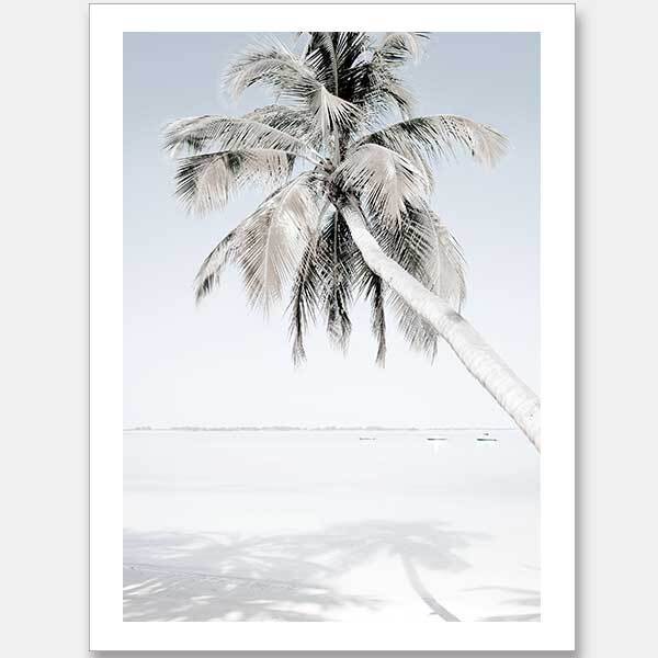 The "Beach Please Unframed Art Print" by Urban Road features a tall palm tree leaning over a sandy beach with calm blue water, capturing a minimalistic and serene coastal scene with the palm's shadow gently cast on the sand.