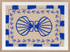 Symmetrical blue shell motif with palm-like flourishes, framed by a blue and cream checkered border on a neutral base, from the Shatha collection with Urban Road.
