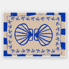 Symmetrical blue shell motif with palm-like flourishes, framed by a blue and cream checkered border on a neutral base, from the Shatha collection with Urban Road.
