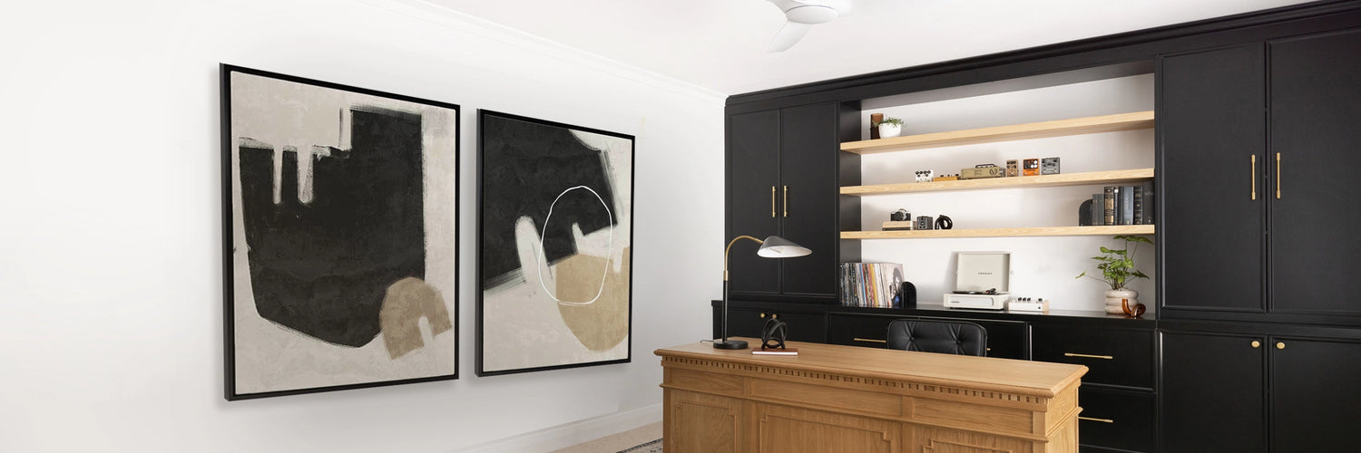 Modern office space with black built-in cabinetry, wooden desk, patterned rug, and two large monochrome artworks.